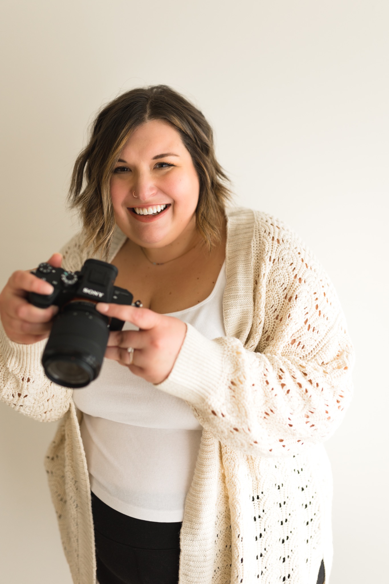 Jess holding her camera in a cream cardigan
