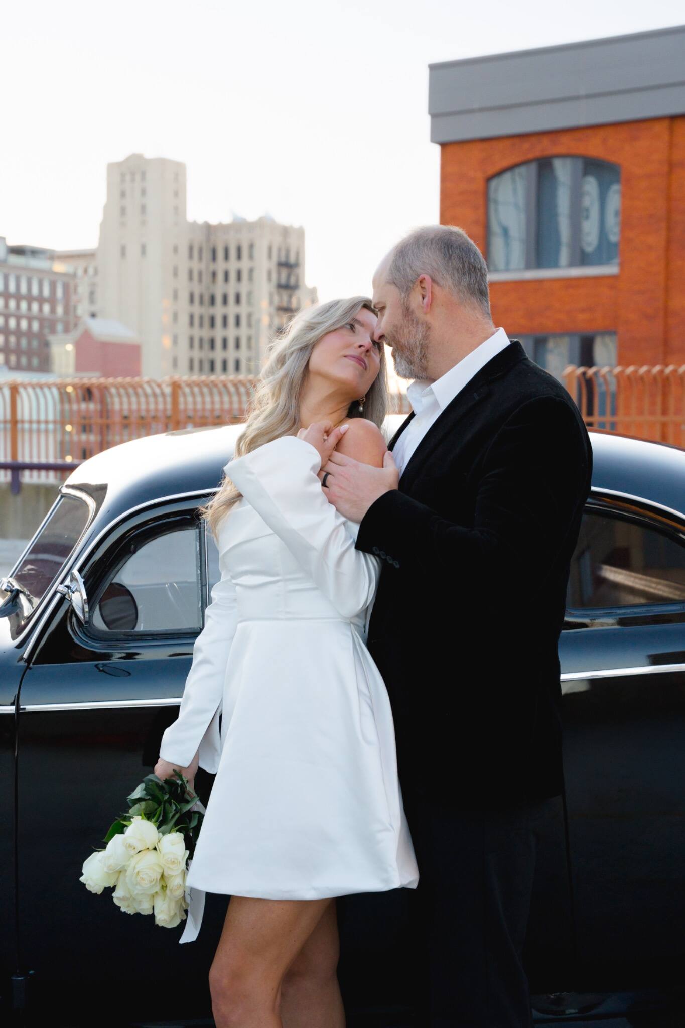 Bride and groom posing beside a vintage car