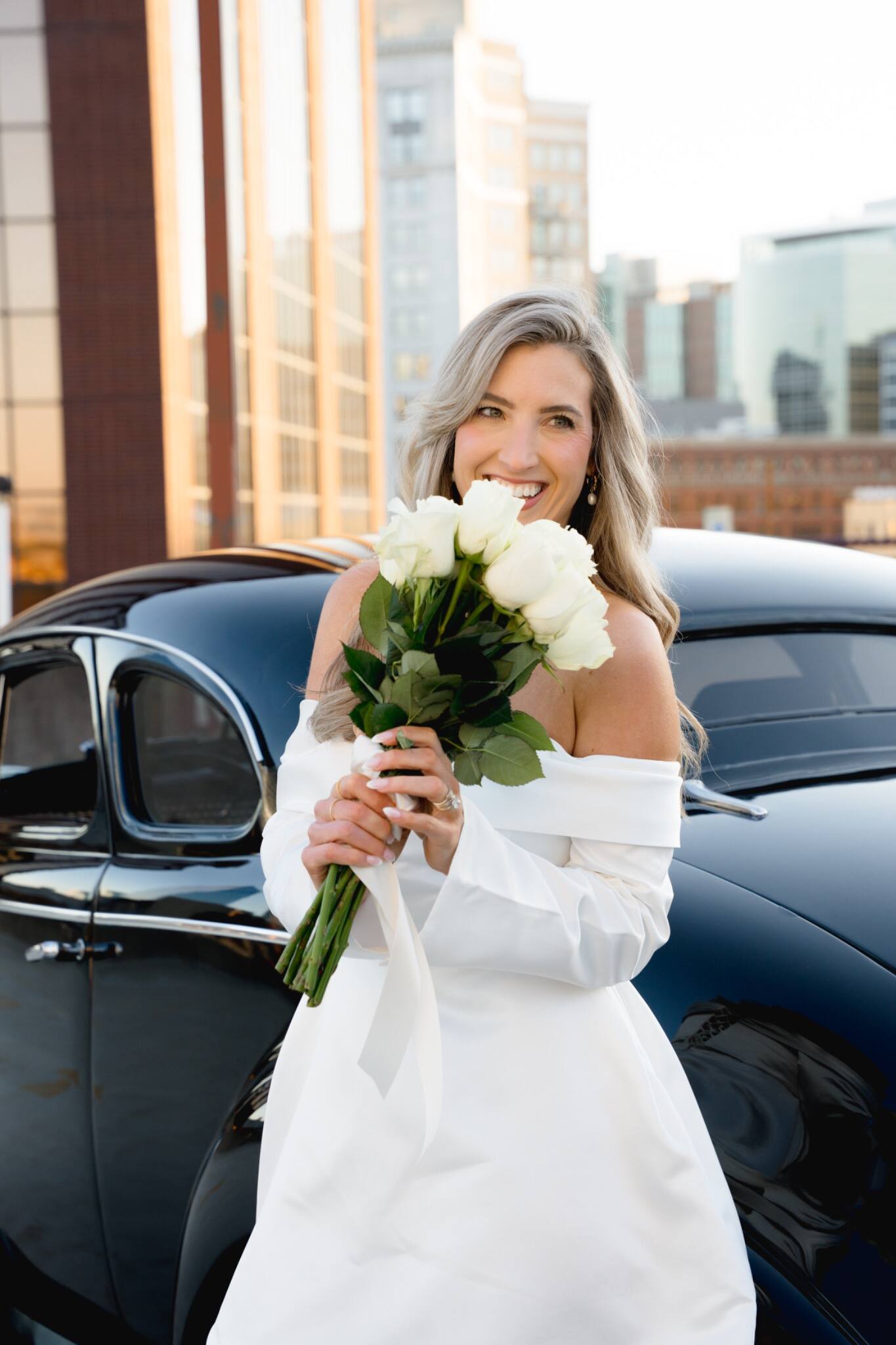 Bride holding her bouquet beside a vintage car