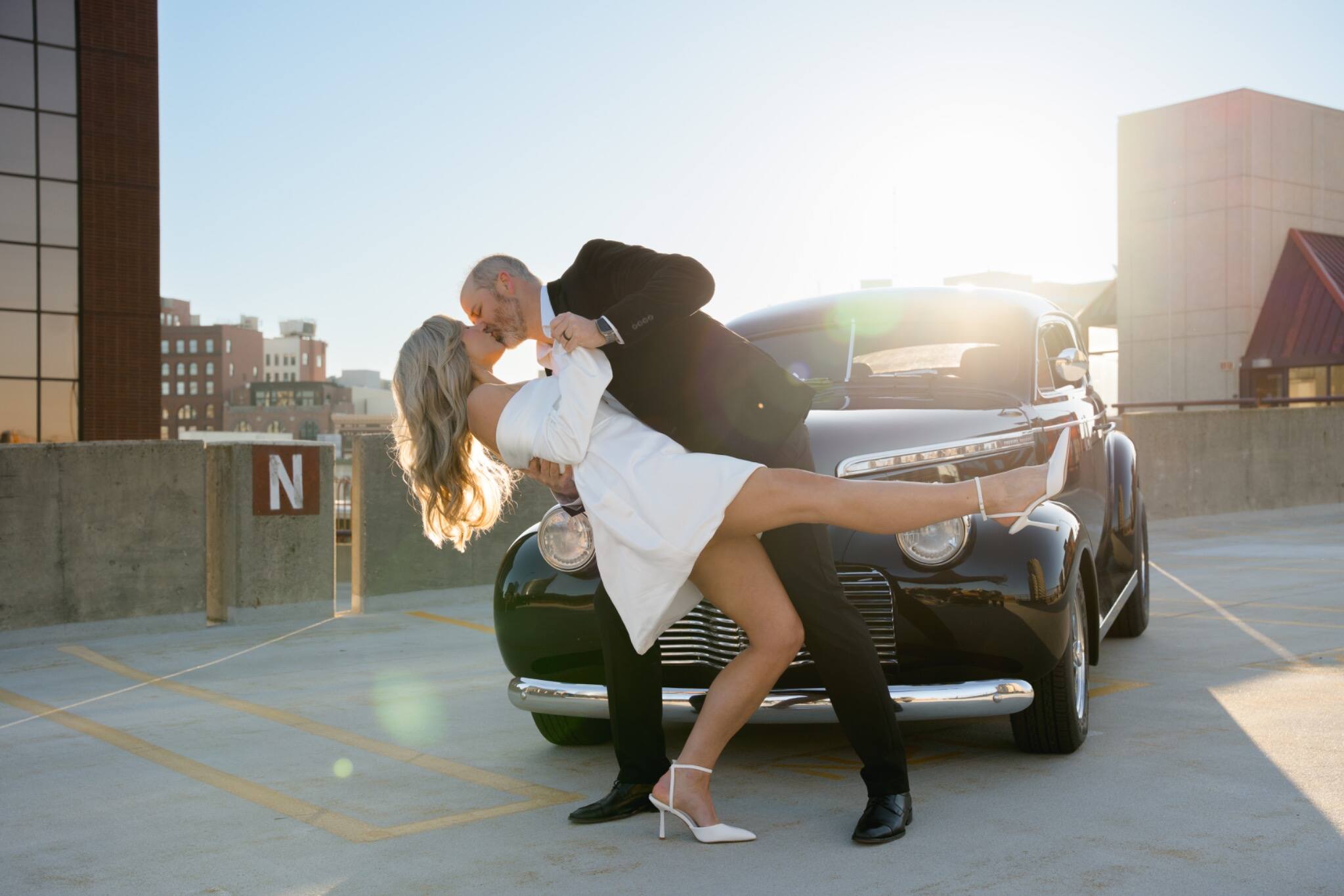 A playful newlywed dip beside a classic car
