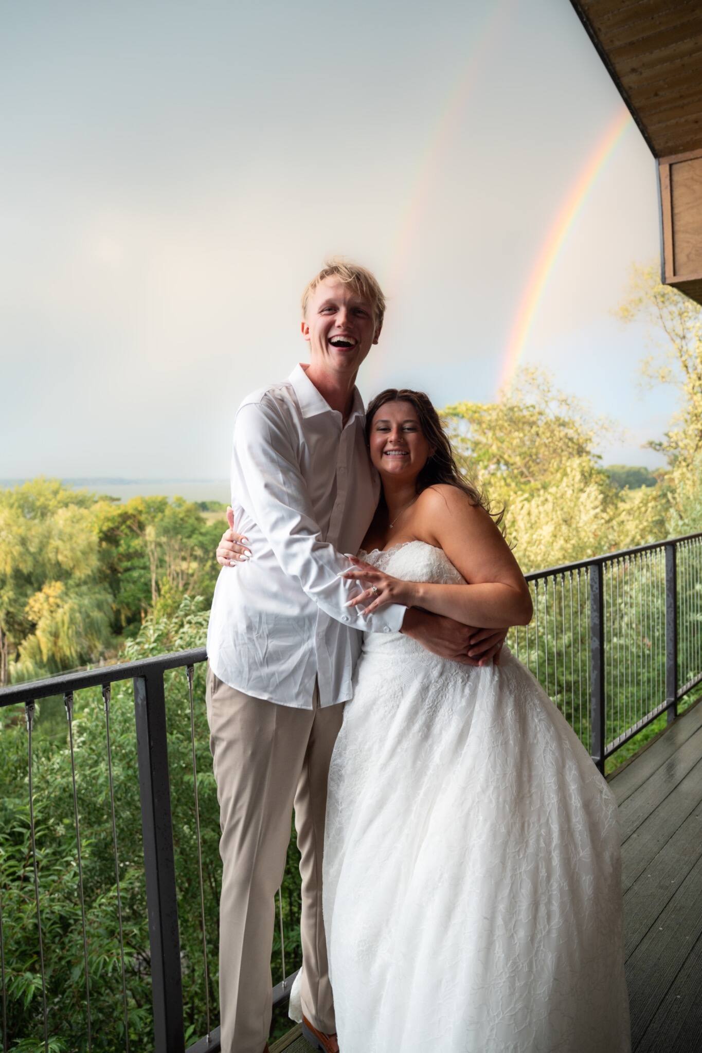 Newlyweds embracing beneath a double rainbow